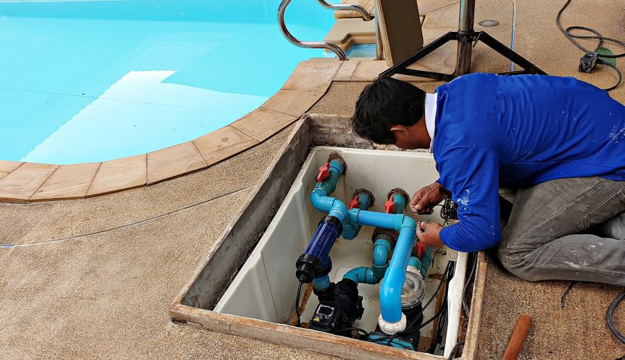 Technician repairing pool pump and plumbing beside a swimming pool
